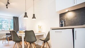 A modern kitchen with white cabinets, a dining table with four chairs, pendant lights, and a view of the outdoors through a window. - Beautiful apartment for 4 guests with WIFI, TV and balcony (Winterberg)