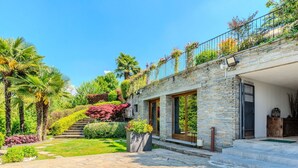Ein modernes Haus mit Natursteinfassade, großen Fenstern und einem gepflegten Garten mit Palmen und Sträuchern.