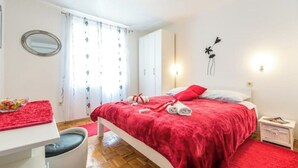 A bedroom with a bed, a bedside table, a chair, a mirror, and a window with curtains.