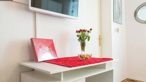 A white desk with a red placemat, a vase with red flowers, and a red book.