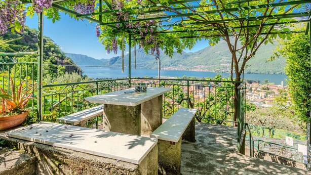 Una terrazza con tavolo e panche che si affaccia su un lago e una città.