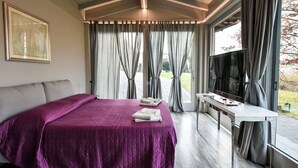 Ein modernes Schlafzimmer mit einem großen Bett, einem Fernseher und Blick ins Freie.