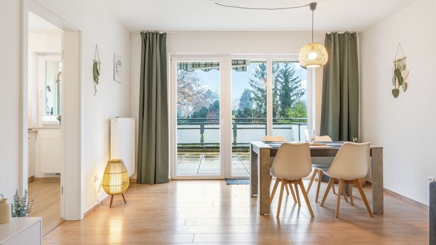 A modern dining area with a table and chairs, a hanging light fixture, and a view through large glass doors to an outdoor balcony. - Cozy barrier-free apartment in central Vegesack/2-4 pers. (Bremen)