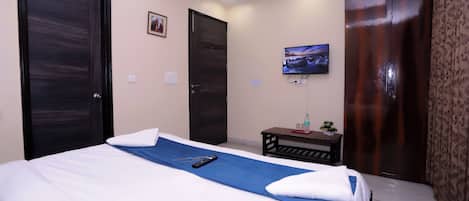 A hotel room with a bed, a TV mounted on the wall, and a wooden wardrobe.