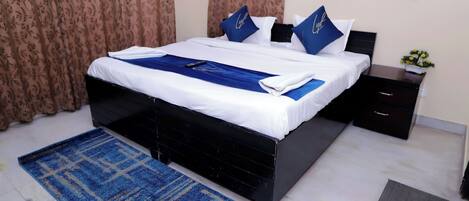 Una cama bien hecha con ropa de cama azul y blanca, una alfombra estampada en azul y blanco, y una mesita de noche con un arreglo floral.