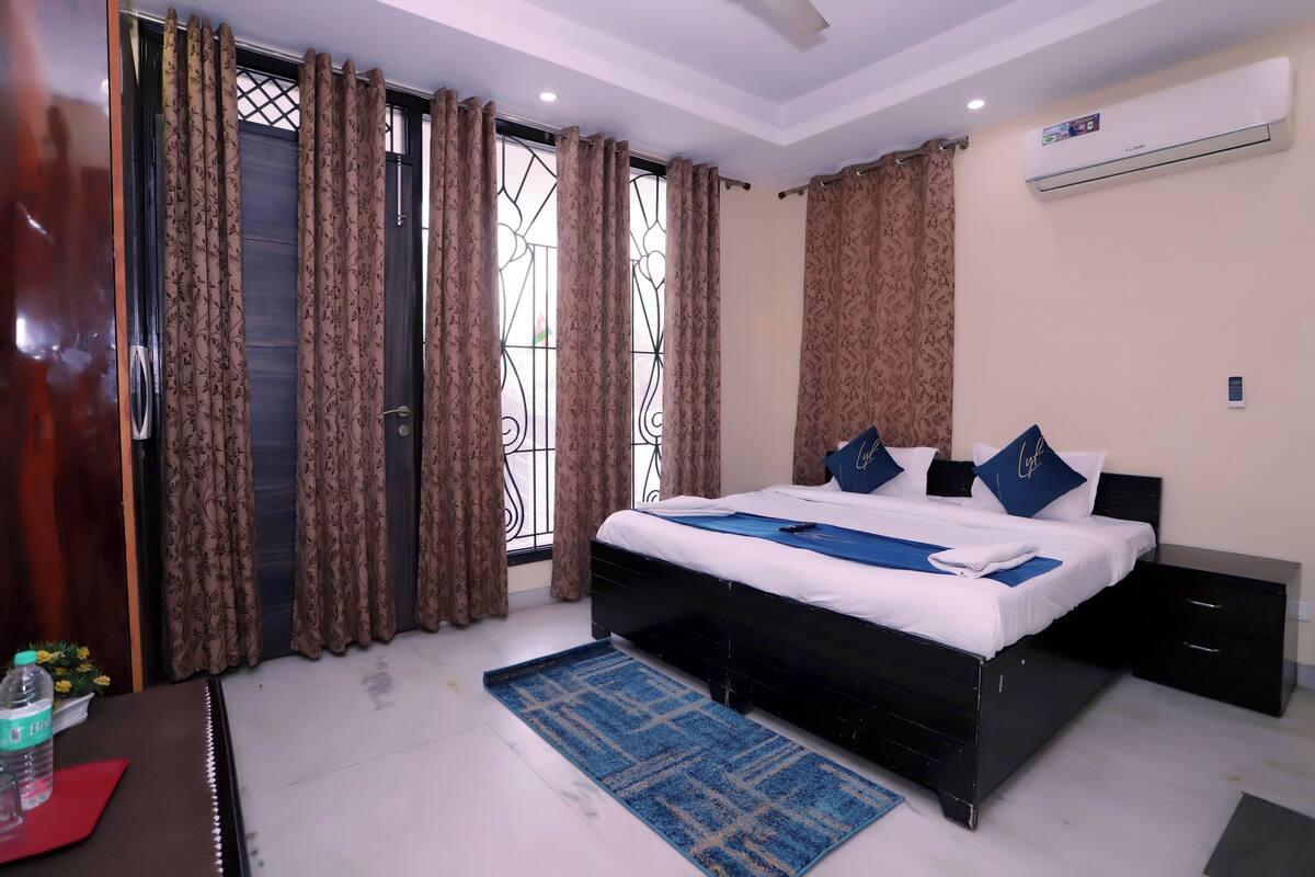 A bedroom with a bed, bedside tables, curtains, and an air conditioning unit.