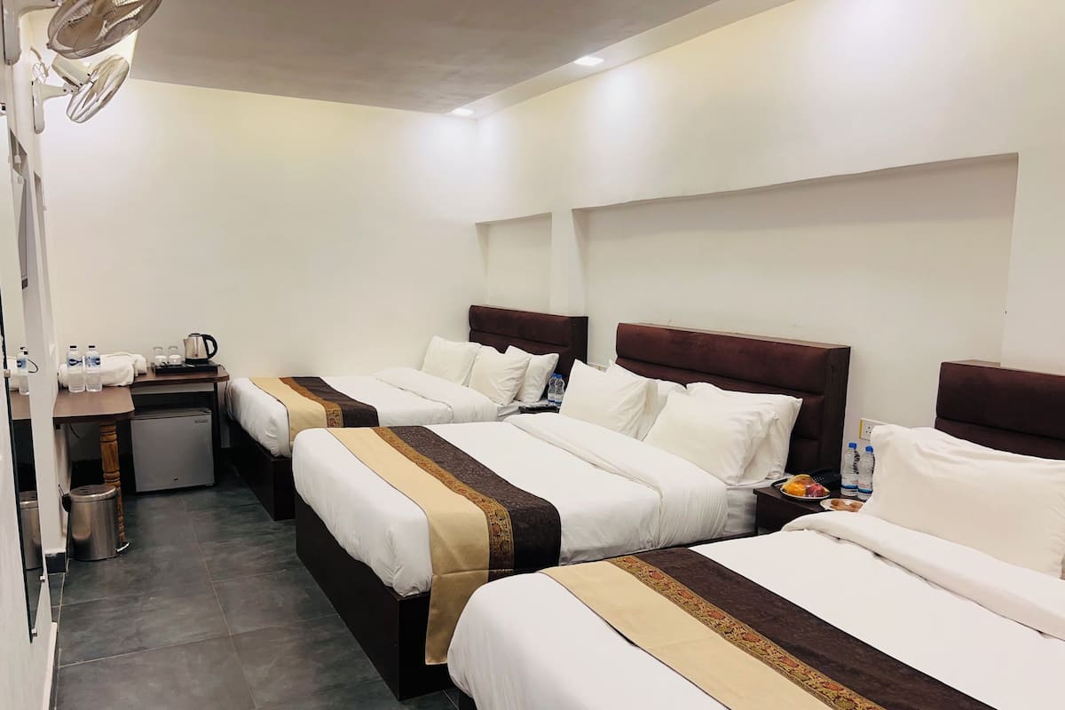 A hotel room with two beds, a desk, a refrigerator, and a trash bin.