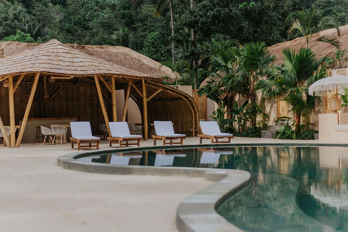 Un área de piscina con sillas de descanso, una estructura de techo de paja y vegetación tropical.