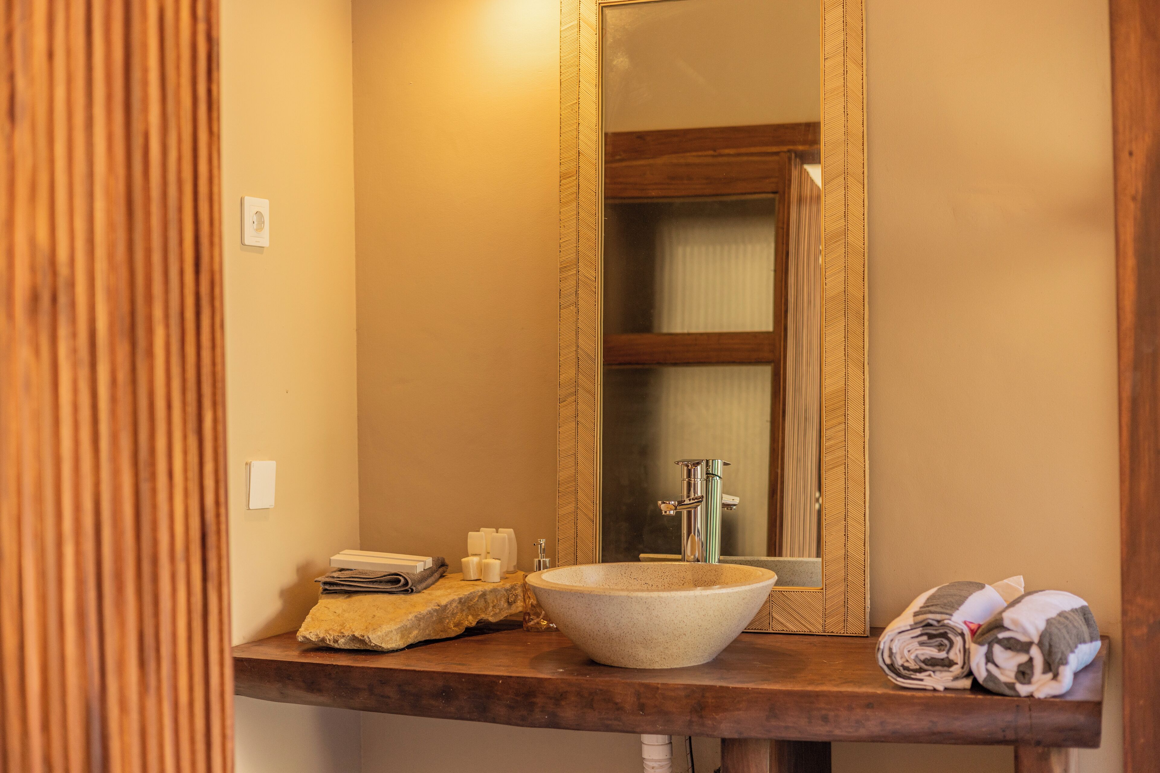 Une salle de bain dotée d’un grand miroir, d’un lavabo en pierre et d’un meuble-lavabo en bois.