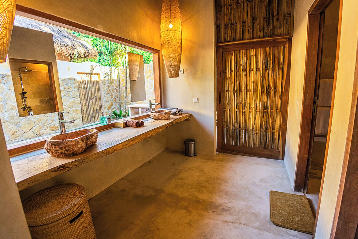 Un baño con pared de piedra, tocador de madera, un espejo grande y puerta de biombo de bambú.