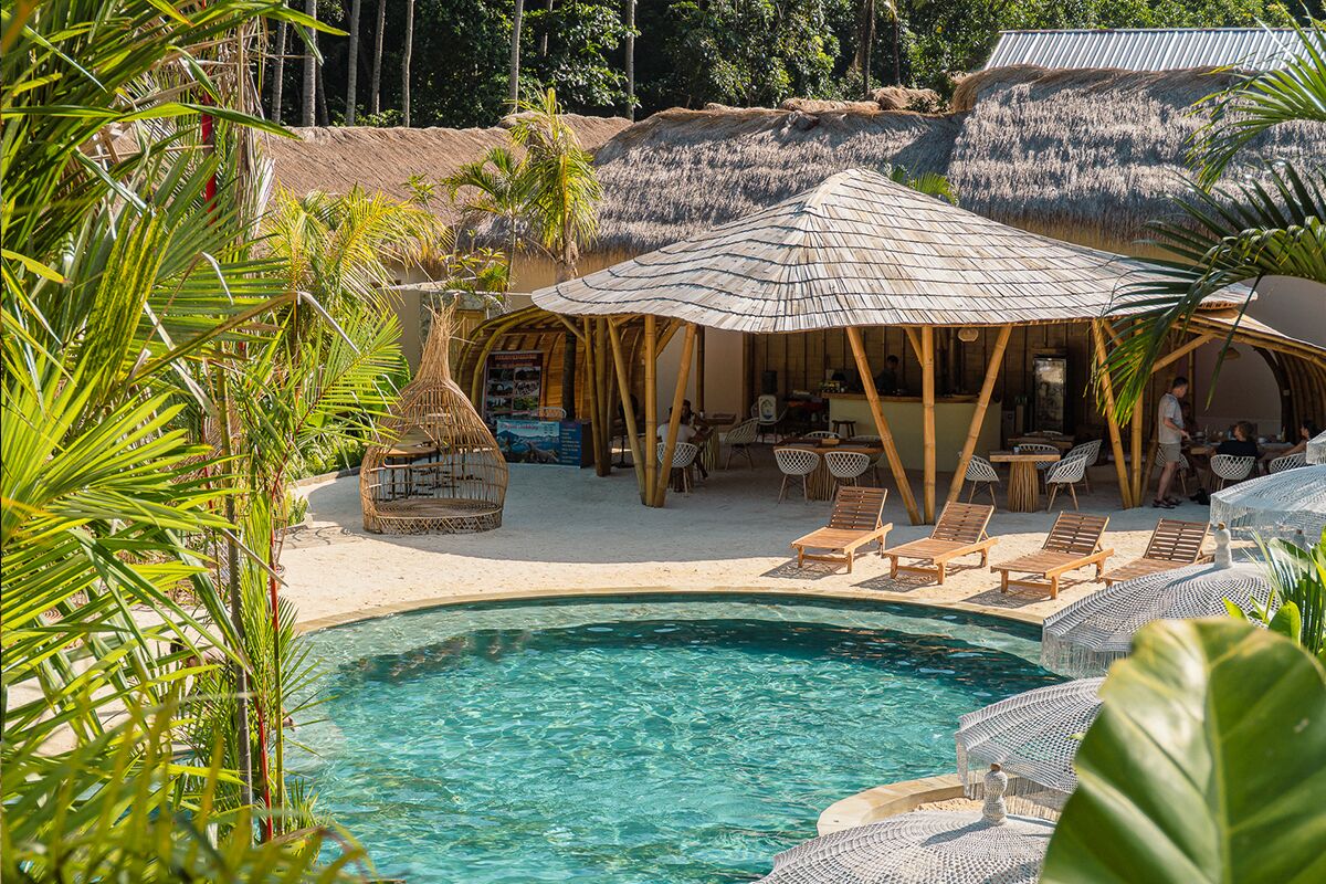 A poolside area with lounge chairs, a thatched-roof structure, and a pool.
