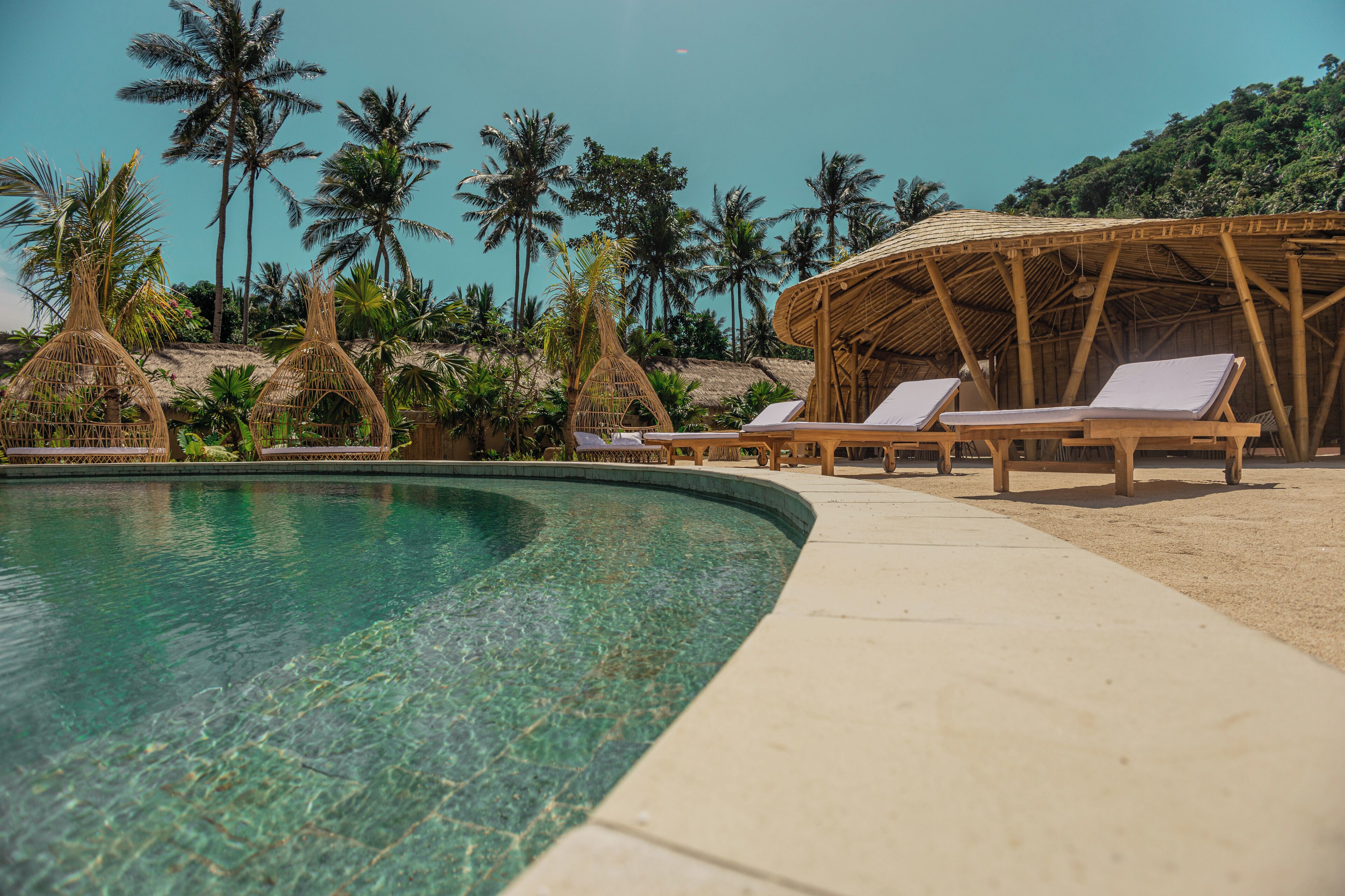 A pool area with lounge chairs and a bamboo structure.