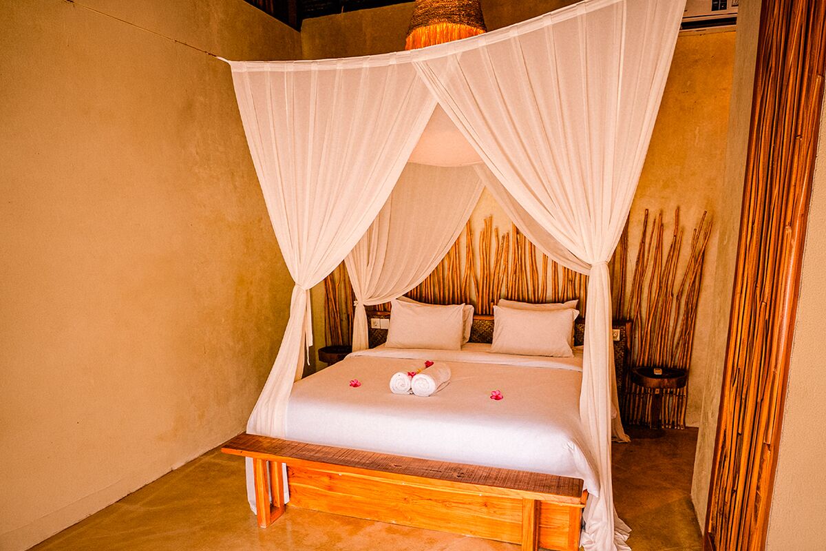 A bed with a canopy, pillows, and a rolled towel on the bed.