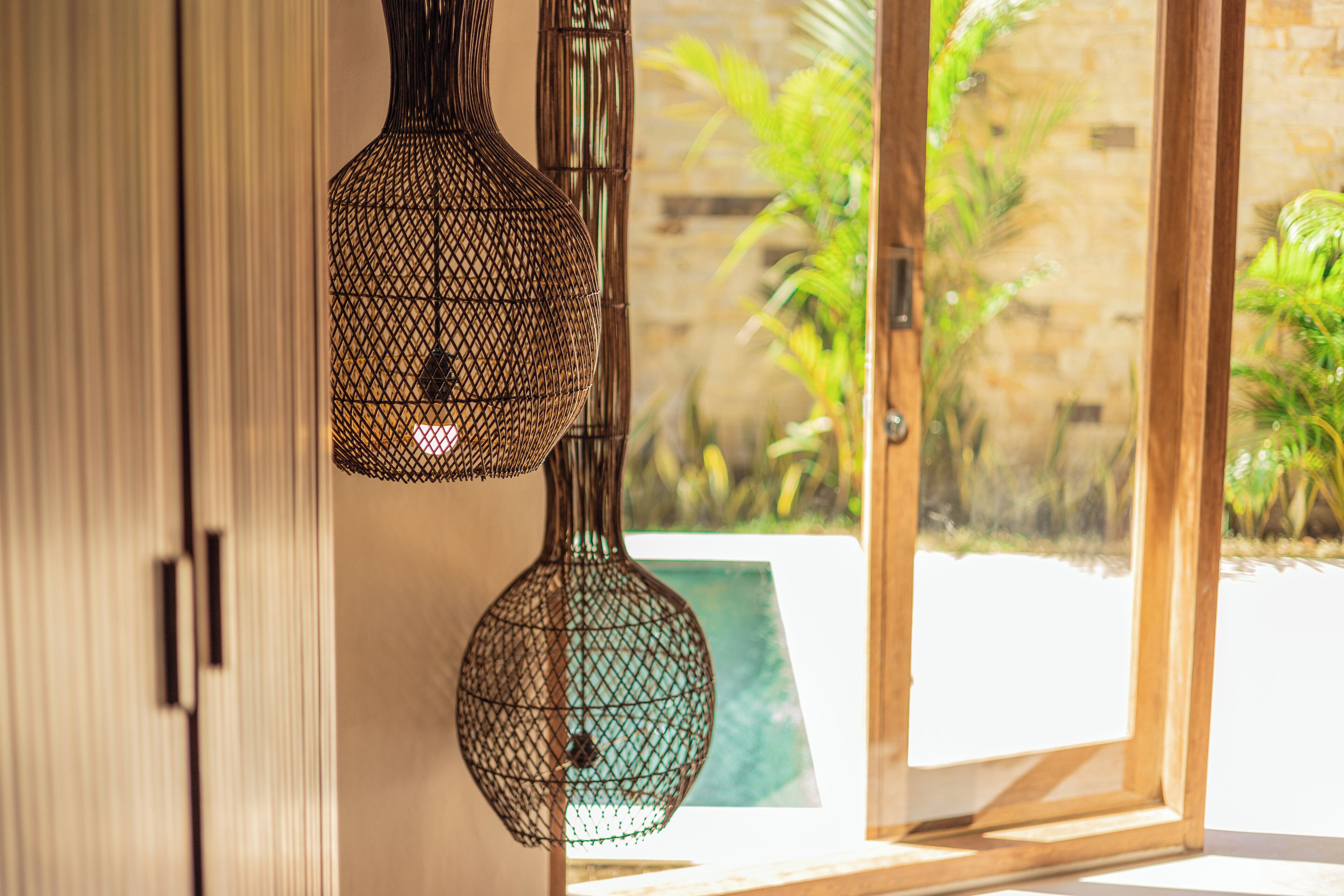 A room with a sliding glass door leading to a garden, a wicker lamp, and a green trash bin.