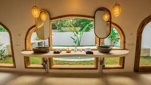 A bathroom with a large mirror, two sinks, and a window with a view of greenery. - Lombok Souls (Senggigi)