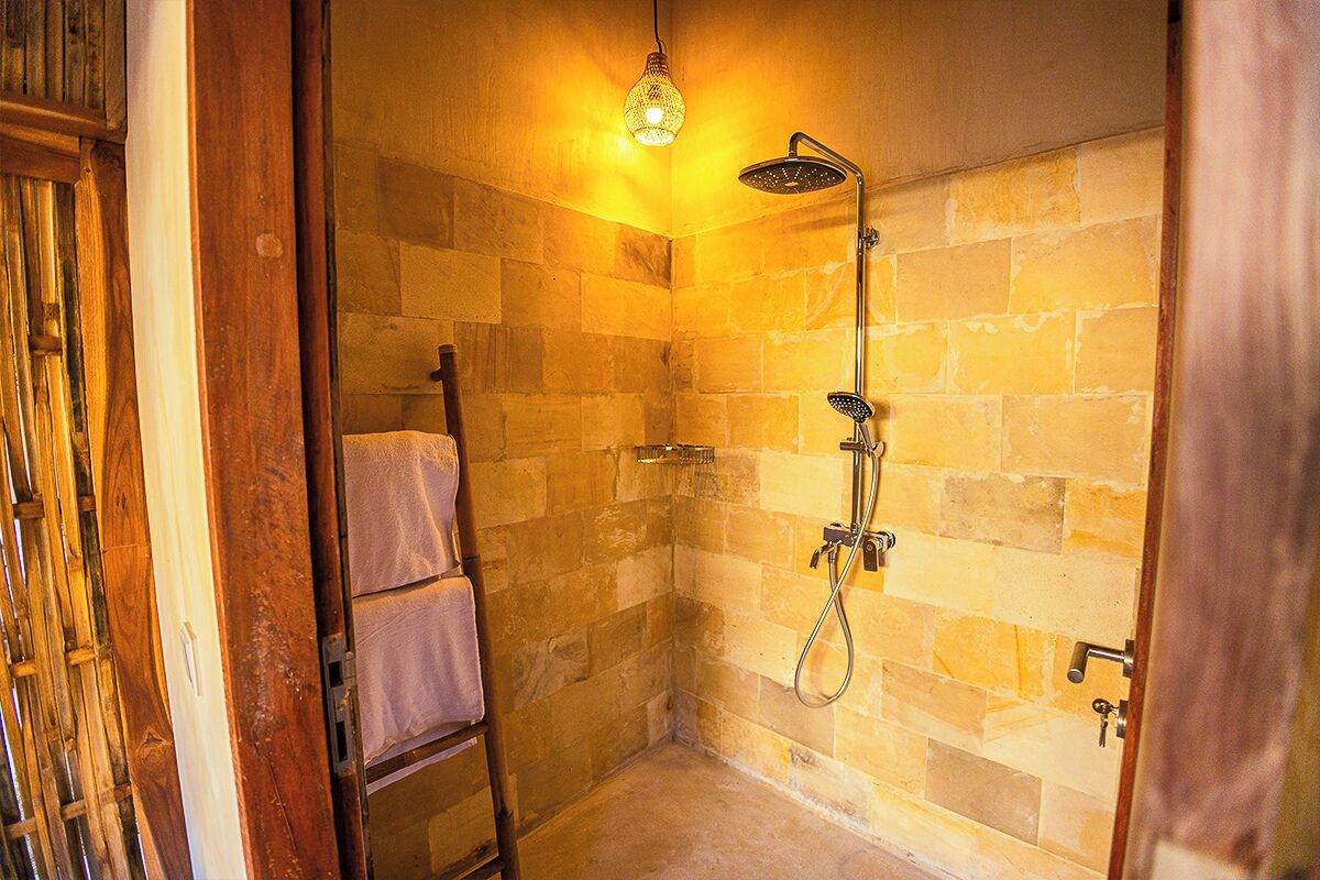 A small, stone-walled shower room with a hanging light fixture, a towel rack, and a showerhead.
