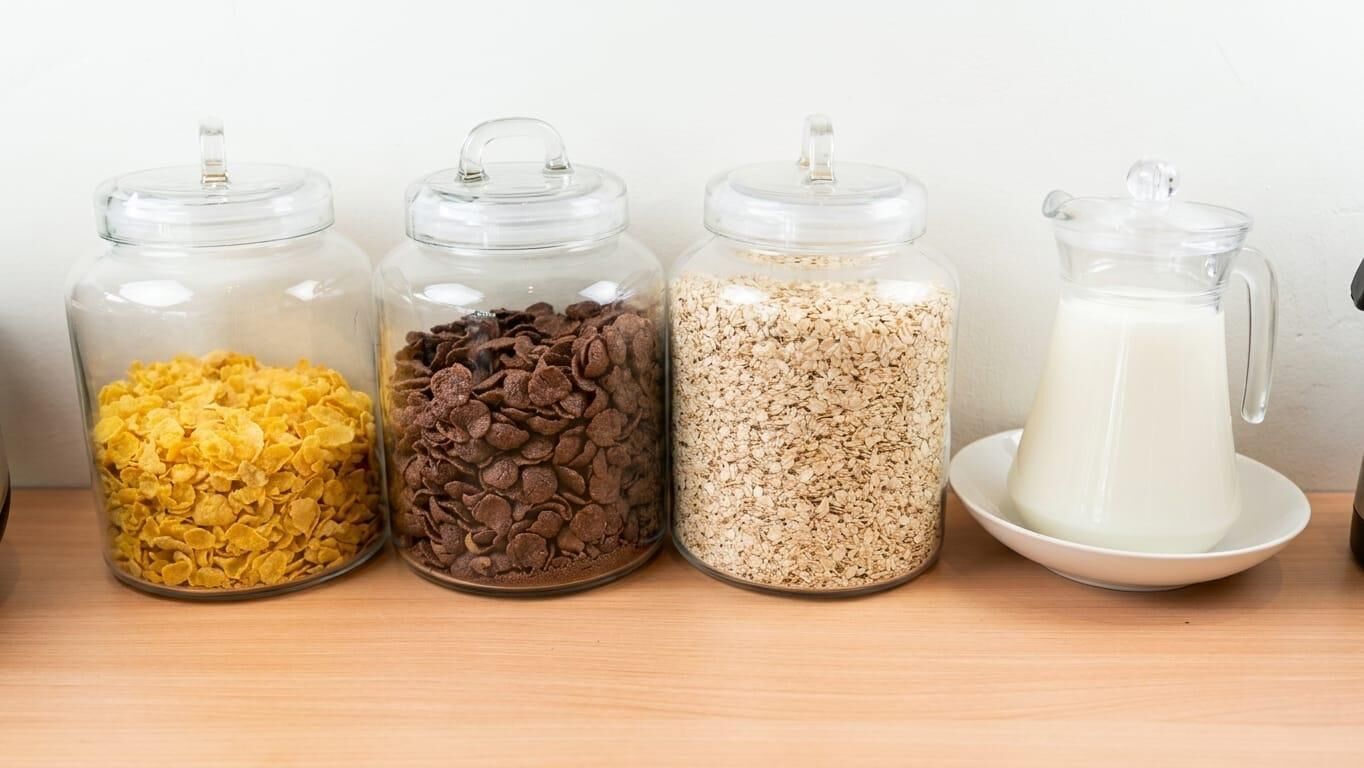 Four glass jars with lids containing different food items on a wooden surface.