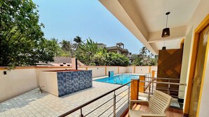 Un área de piscina en la azotea con piso de baldosas, piscina azul y terraza de madera.