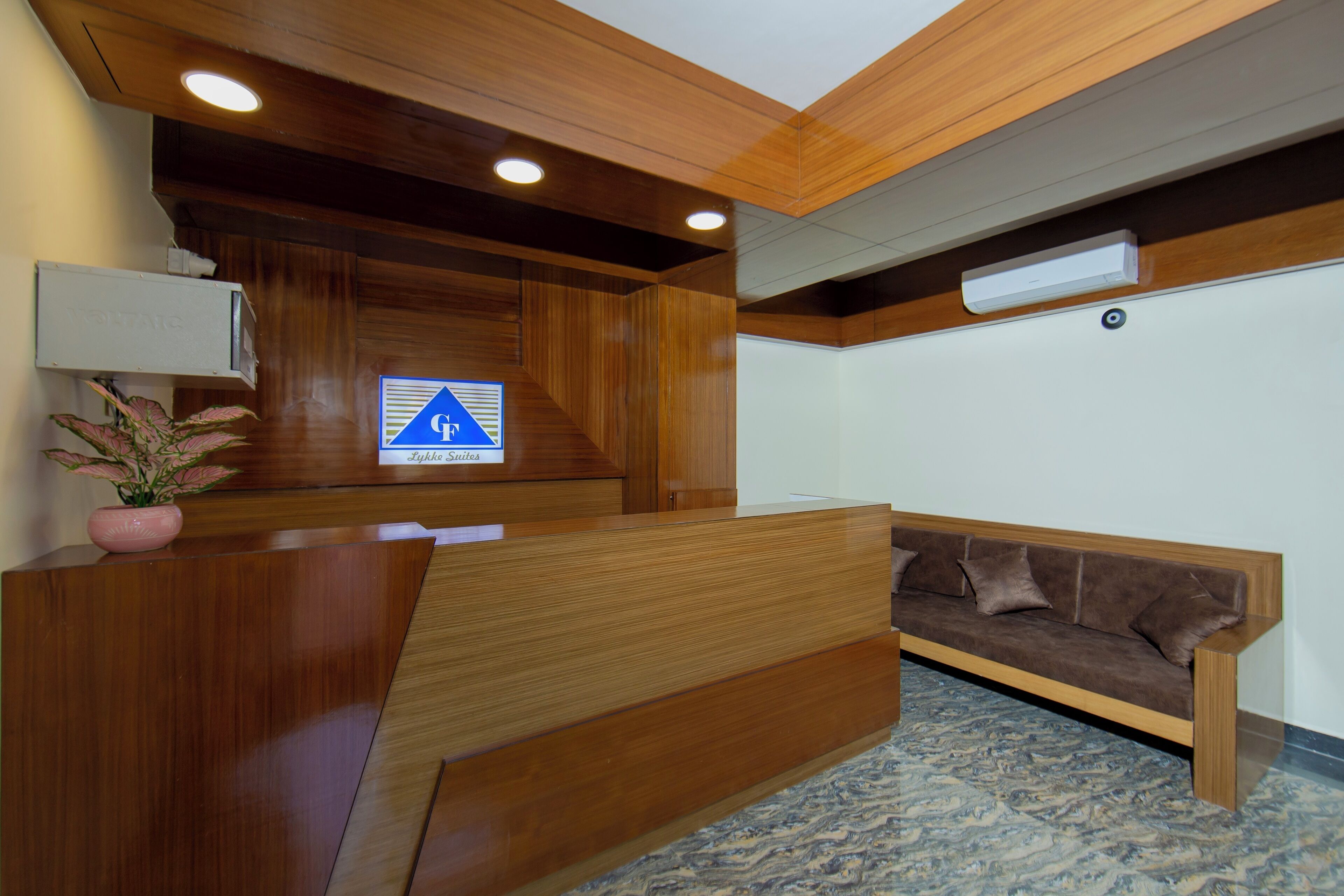 A reception desk with a wooden finish, a potted plant, and a sign indicating "Lykke Suites".