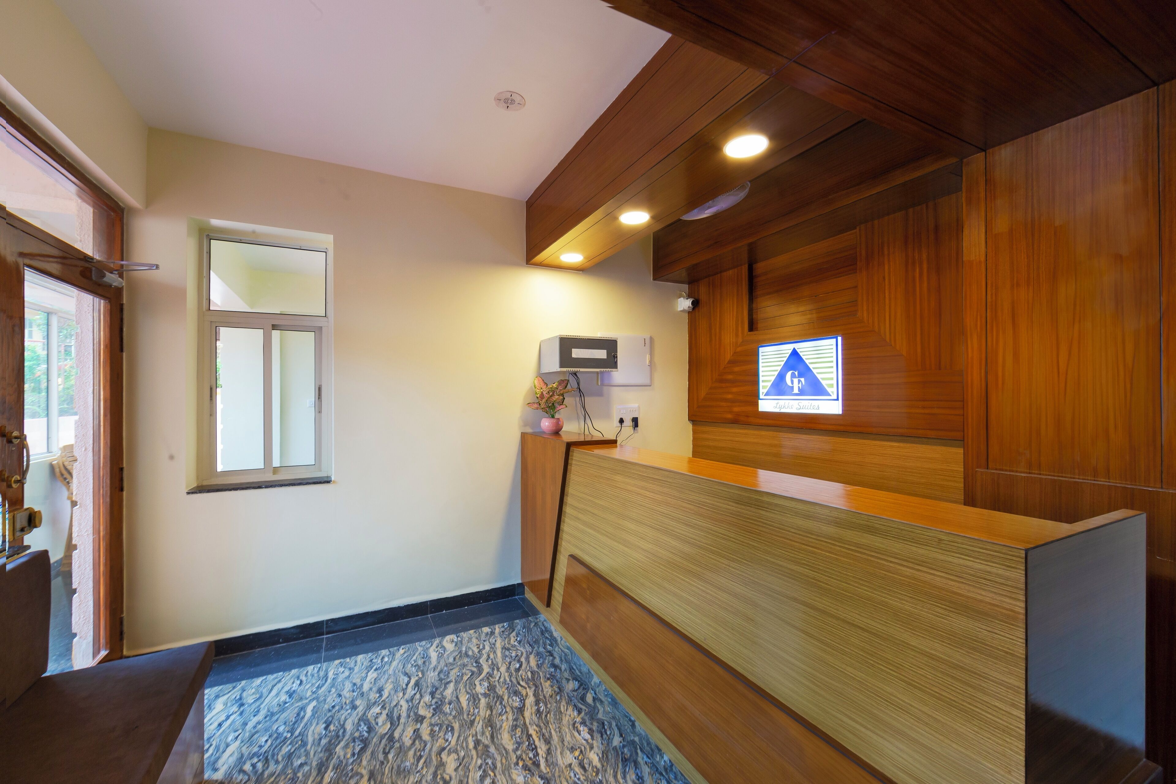 Un área de recepción con un mostrador de madera, una unidad de aire acondicionado pequeña y un cartel indicativo en la pared.