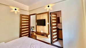 Un dormitorio con cama, televisor montado en un panel de madera y un ba ño visible a través de una puerta abierta.