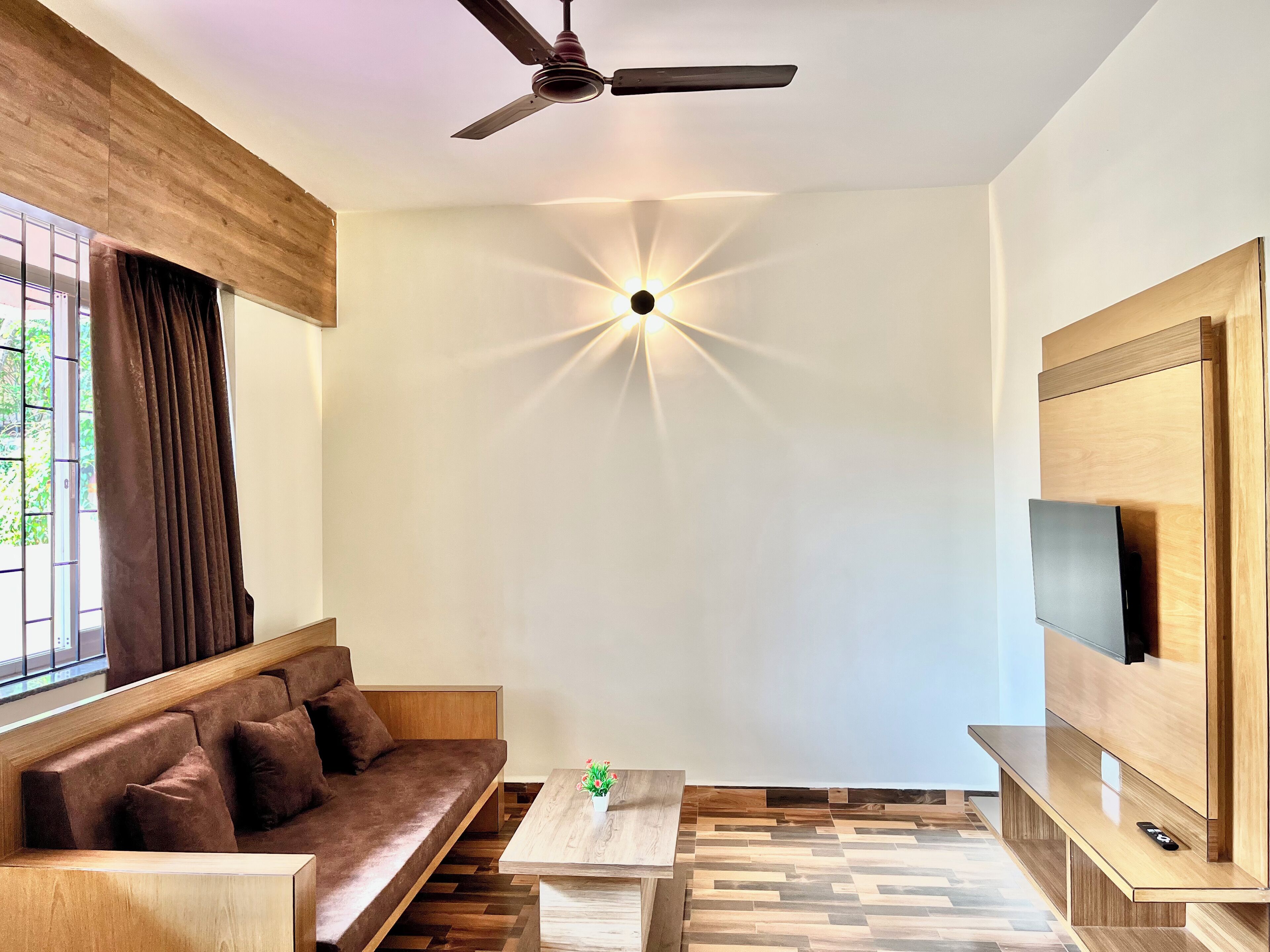 Una sala de estar moderna con un sofá, una mesa de centro, un televisor montado en la pared y un ventilador de techo.