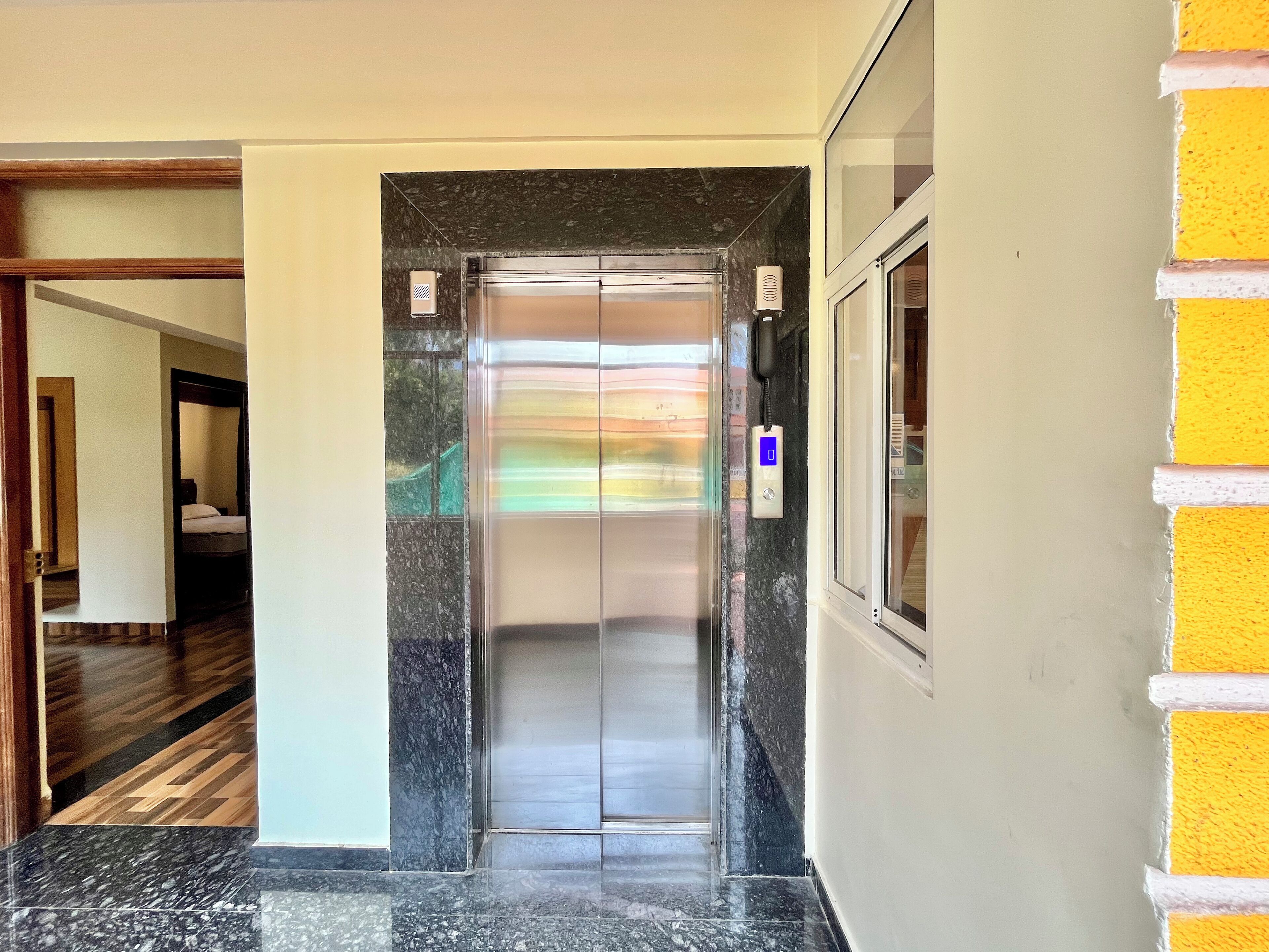 Un ascensor en el vestíbulo de un hotel, con piso de mármol y marco de puerta de madera.