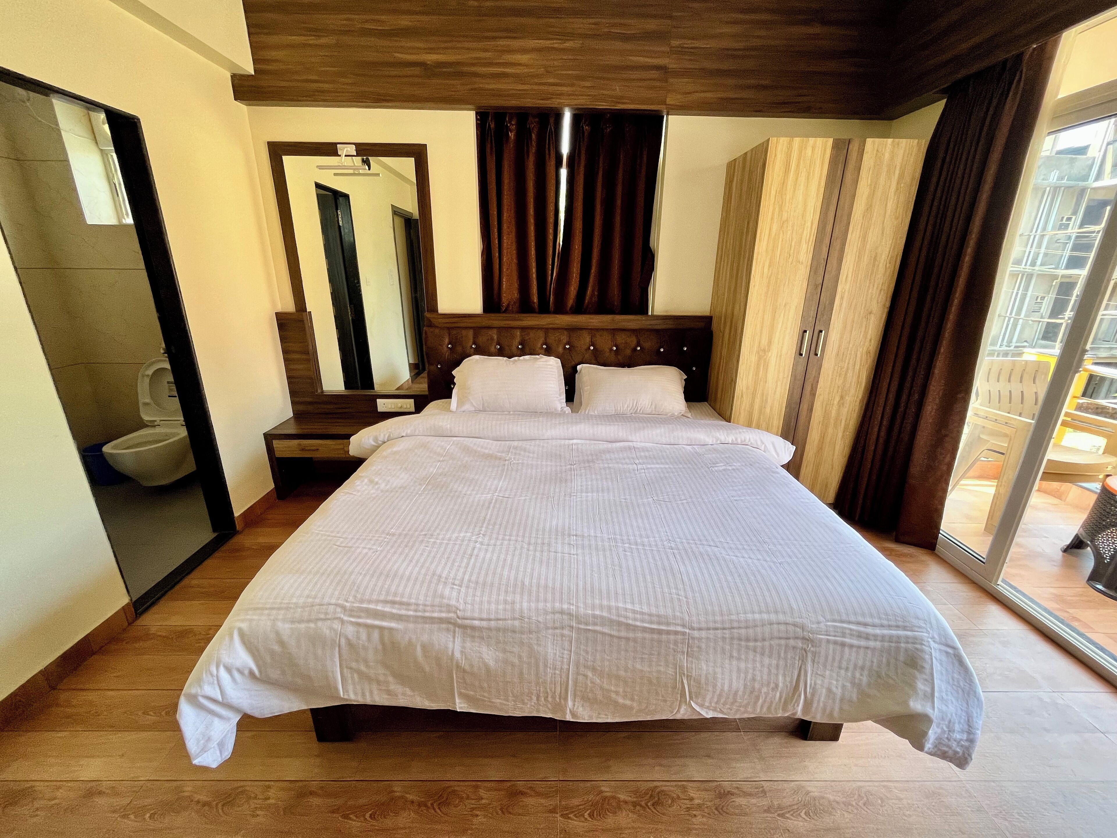 Un grand lit avec une tête de lit en bois, un miroir et une vue sur l’extérieur par une fenêtre.