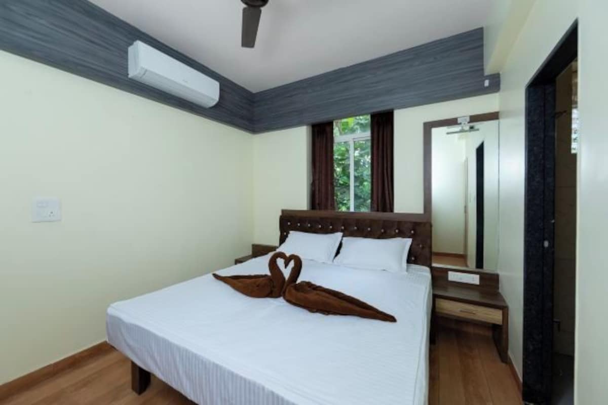 Una habitación de hotel con cama, mesita de noche, espejo y ventana con cortinas.
