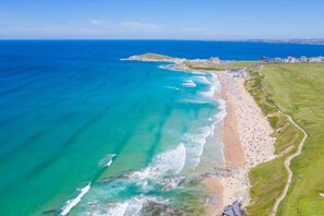 Vista aérea de una zona costera con playa, una pequeña isla y edificios a lo lejos.