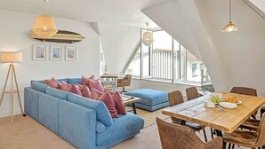 A modern loft apartment with a blue sofa, dining table, and large windows offering a view of the outside.