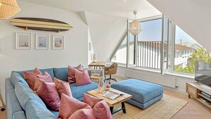 A modern living room with a blue sofa, pink cushions, a wooden coffee table, and a TV on a wooden stand.