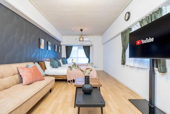 Un salon moderne avec un canapé, une table basse agrémentée d’un vase, un lit offrant une belle vue et un téléviseur à écran plat affichant le logo de YouTube.