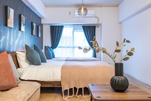Une chambre moderne avec un lit, un canapé, une table de chevet en bois, un vase avec des plantes et une fenêtre avec des rideaux.