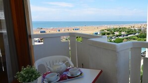 Un balcón con una mesa dispuesta para tomar té, una planta en maceta y vista a la playa y al mar.