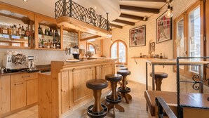 Angolo bar con sgabelli di legno, un bancone pieno di bottiglie e una scala.