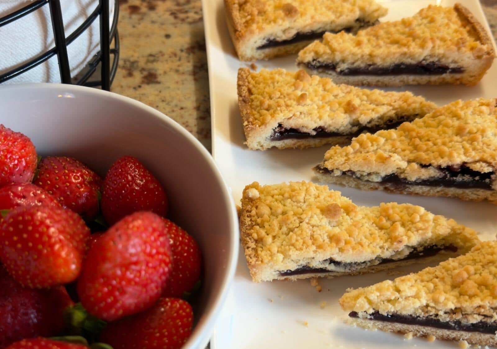 A tray of dessert bars with a crumbly topping and a bowl of fresh strawberries.