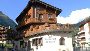 Un edificio tradizionale in legno con balconi, un cartello con la scritta "Bar Restaurant Le Mazot" e montagne sullo sfondo.