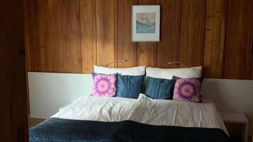 Ein Schlafzimmer mit Holzboden, einem Bett mit weißem Kopfteil und einem gerahmten Bild an der Wand.