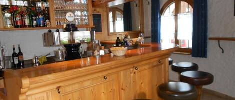 Un espace bar doté d’un comptoir en bois, de tabourets et d’une variété de bouteilles et de verres.