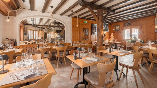Un ristorante con tavoli e sedie in legno, un soffitto alto con travi a vista e lampadari appesi.