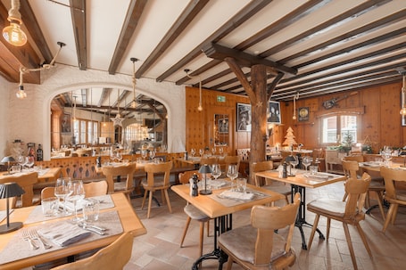 A restaurant with wooden tables and chairs, a high ceiling with exposed beams, and hanging light fixtures.