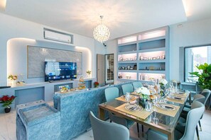 Un comedor moderno con una larga mesa dispuesta para una comida, un televisor montado en la pared y una lámpara decorativa.