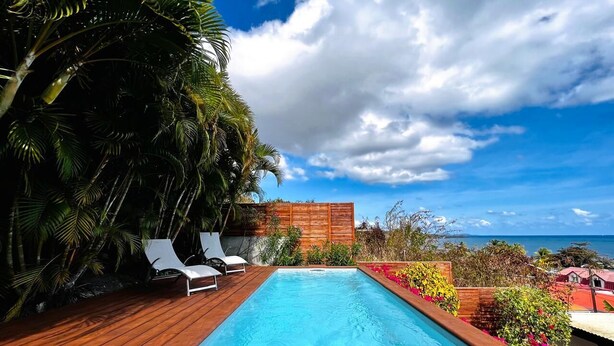 A rectangular pool with a wooden deck, two white lounge chairs, and a wooden fence. - Martinique Villa Escale Diamant (Le Diamant)