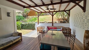 A covered patio with a wooden table and chairs, a sofa, and a view of a garden. - Martinique Villa Escale Diamant (Le Diamant)