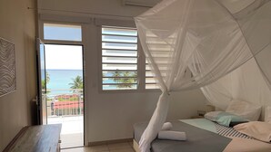 A bedroom with a bed, a bench, a window with blinds, and a view of the sea. - Martinique Villa Escale Diamant (Le Diamant)