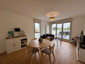 Un salon moderne avec un coin repas, de grandes fenêtres et une vue sur l’extérieur.