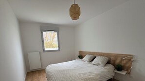 Ein Schlafzimmer mit Bett, Fenster, Heizkörper und einer Hängeleuchte.