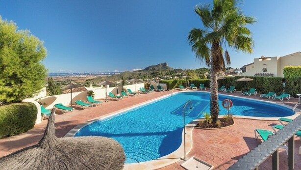 Piscina con sillas de descanso y una palmera, rodeada de jardines con vistas a colinas distantes.