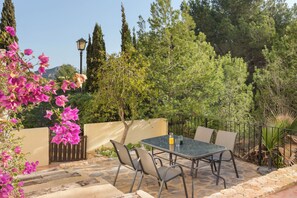 An outdoor patio with a table and chairs, surrounded by greenery and a stone wall. - Quiet ground floor 3 bedroom apartment - private patio -  pools with jacuzzi (Atamaria)